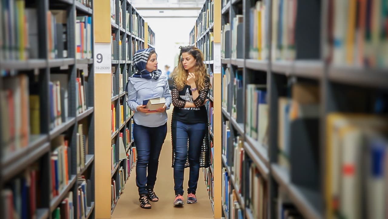 Two female students discussing while walking in library