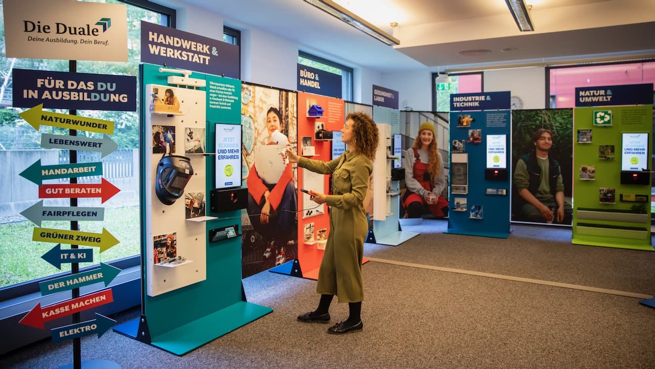 A woman interacts with a display panel in the section ‘Handwerk & Werkstatt’ in an exhibition space on vocational training